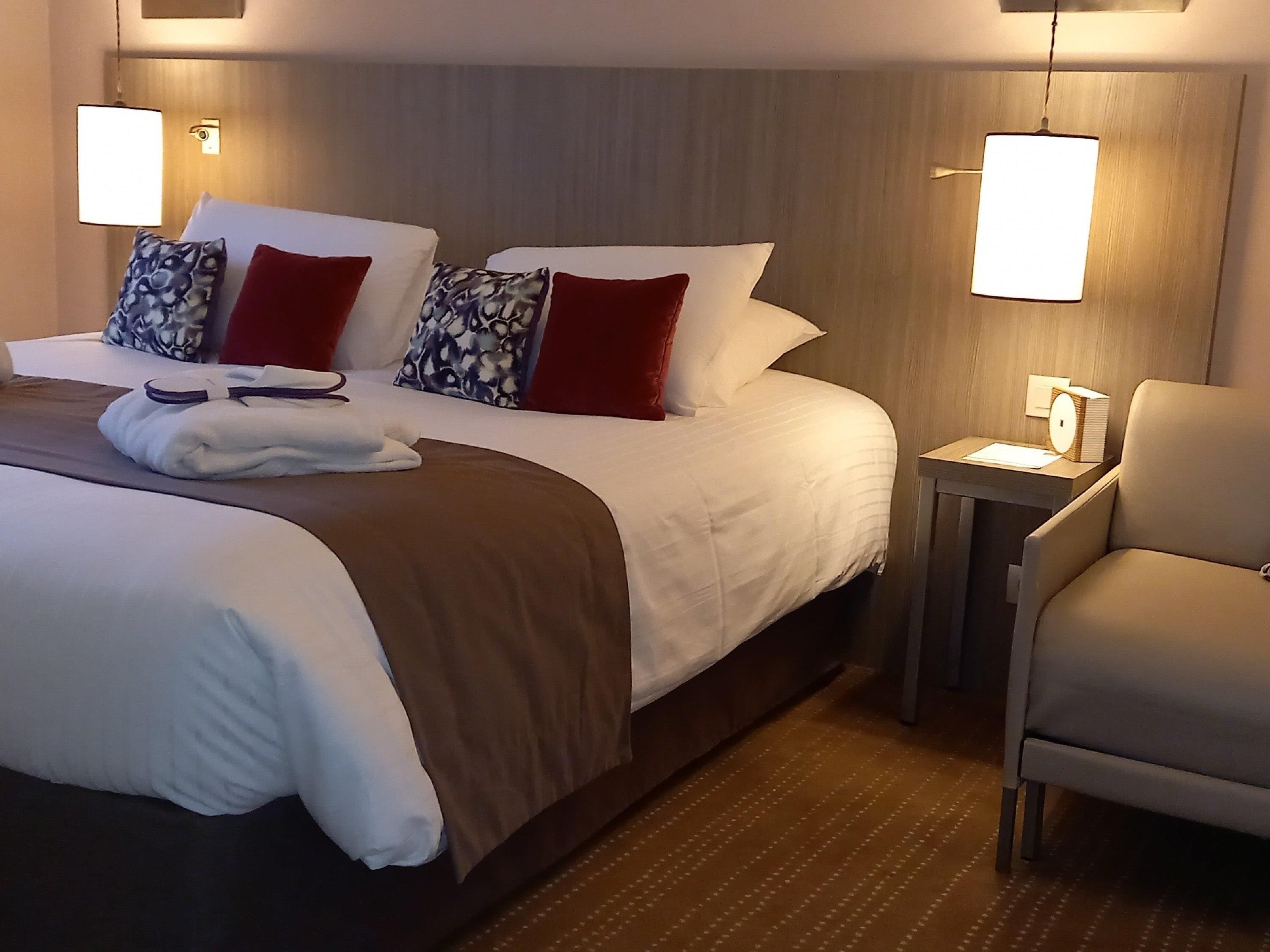 Een hotelkamer met een groot bed, twee nachtkastjes, een stoel en een wandlamp.
