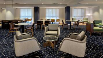 A hotel lobby with a dining area, seating arrangements, and a carpeted floor.