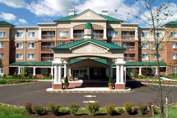 A multi-story hotel with a central entrance, a green roof, and a landscaped driveway.