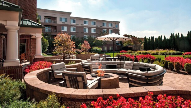 A circular outdoor seating area with fire pit, surrounded by lush flower beds and a large umbrella. - Courtyard by Marriott Basking Ridge (Basking Ridge)