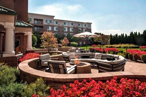 A circular outdoor seating area with fire pit, surrounded by lush flower beds and a large umbrella. - Courtyard by Marriott Basking Ridge (Basking Ridge)