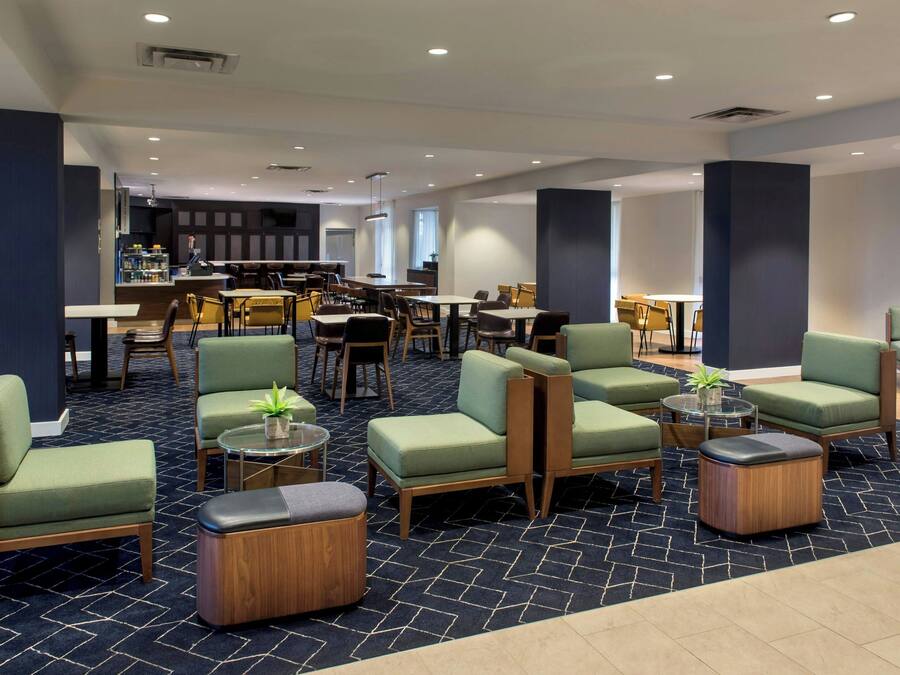 A hotel lobby with green upholstered seating, a bar area, and a patterned carpet.