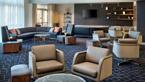 A modern hotel lobby with a sectional sofa, armchairs, ottomans, a round coffee table, and a flat-screen TV mounted on the wall. - Courtyard by Marriott Basking Ridge (Basking Ridge)