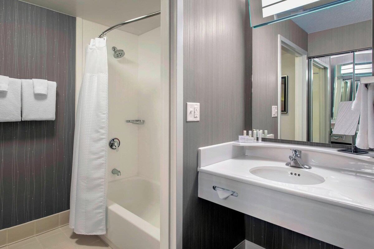 Un baño moderno con ducha, lavamanos con espejo y un perchero para toallas.