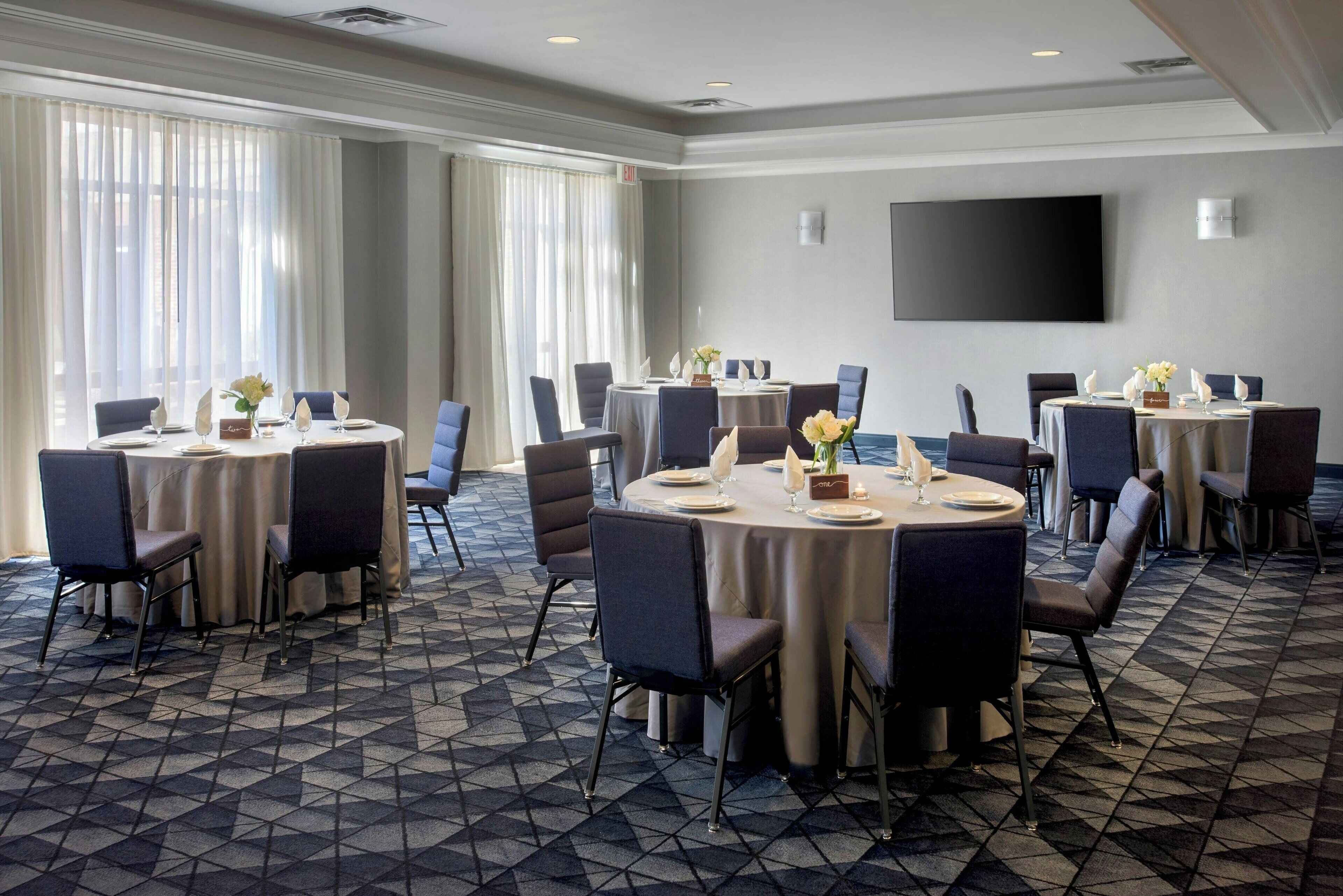 A conference room with multiple tables, chairs, and a large flat-screen TV on the wall.