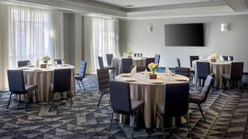 A conference room with multiple tables, chairs, and a large flat-screen TV on the wall.