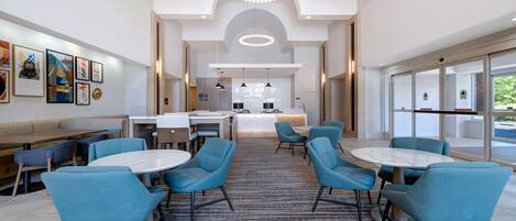 A modern hotel lobby with round tables, blue chairs, and a reception desk.