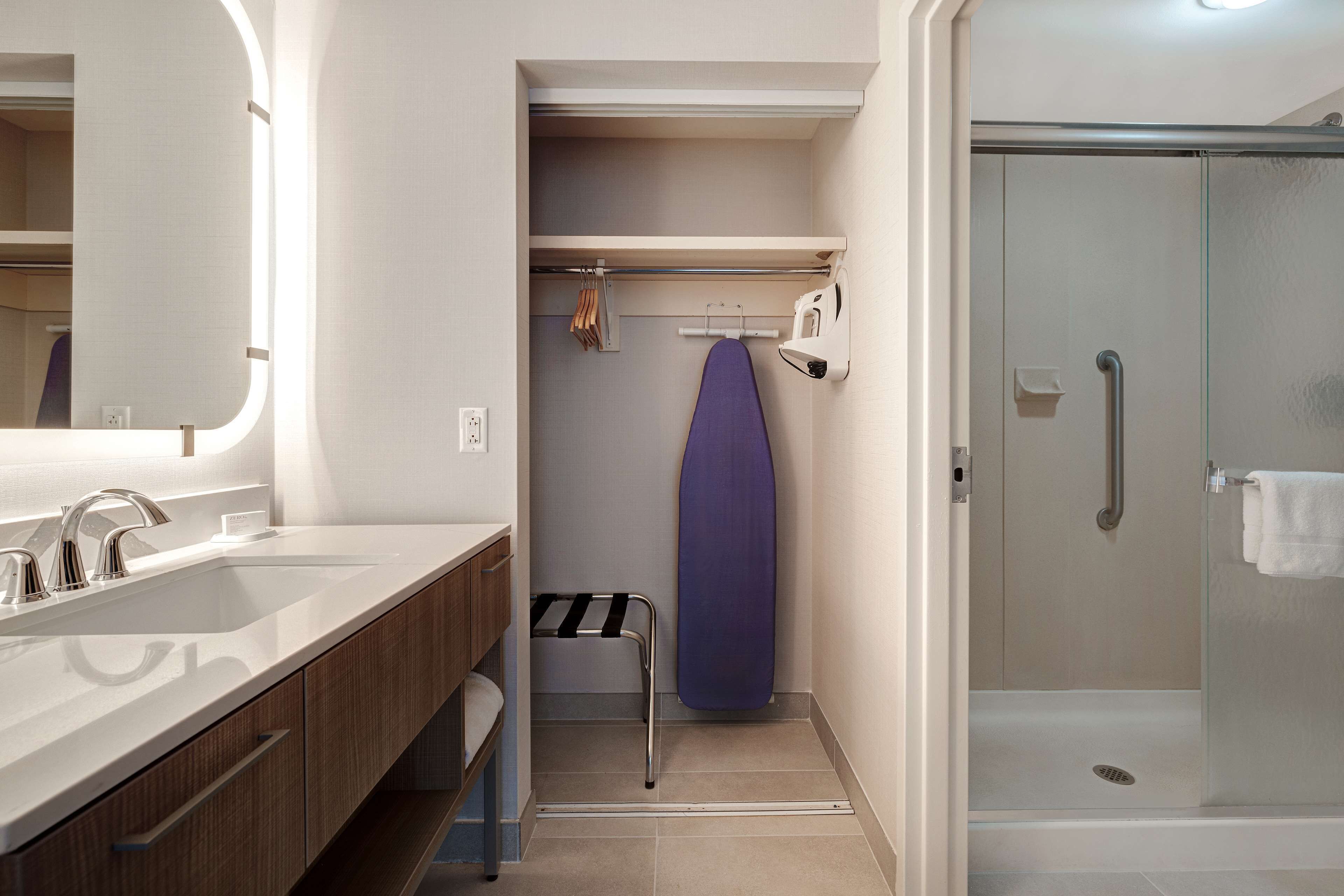 Une salle de bain équipée d’un lavabo, d’un miroir, d’une douche et d’une planche à repasser.