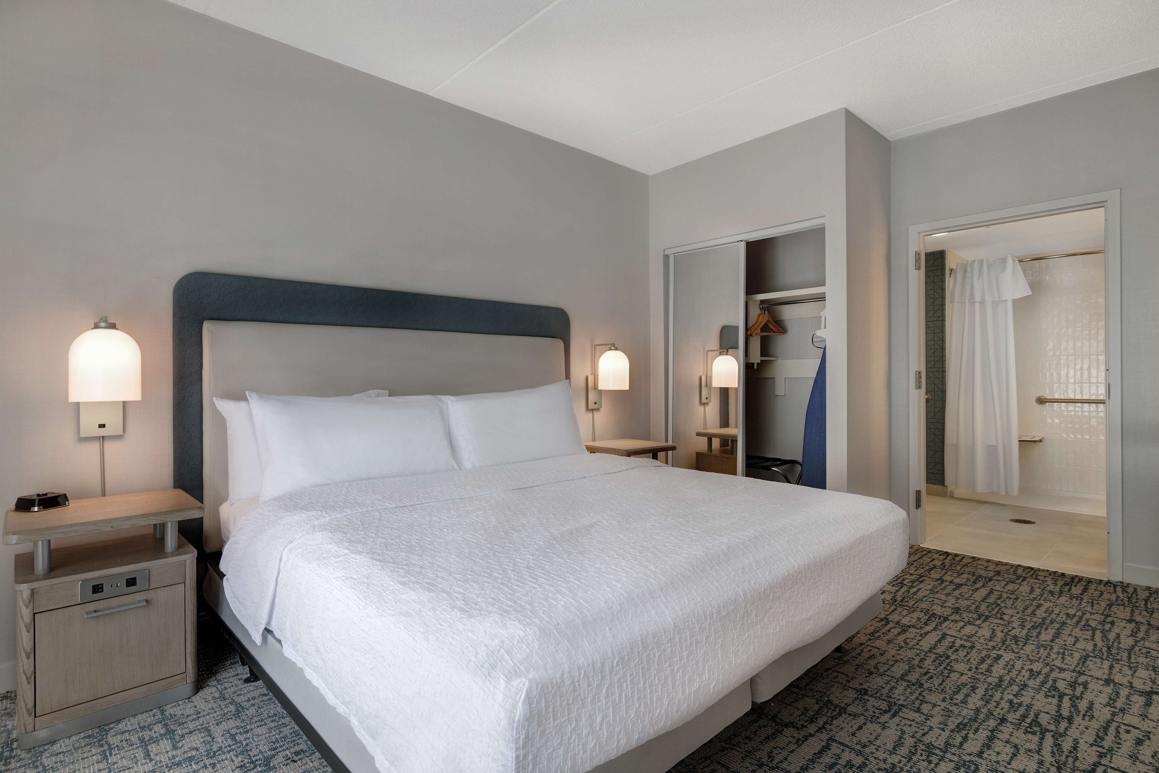 Una habitación de hotel con una cama grande, mesitas de noche, un armario y una zona de ducha.