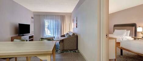 A hotel room with a bed, a desk, a television, a sofa, and a window with curtains.