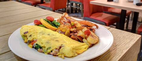 Une assiette de nourriture comprenant une omelette, des pommes de terre et des fraises, posée sur une table en bois dans un restaurant aux chaises et aux tables rouges.