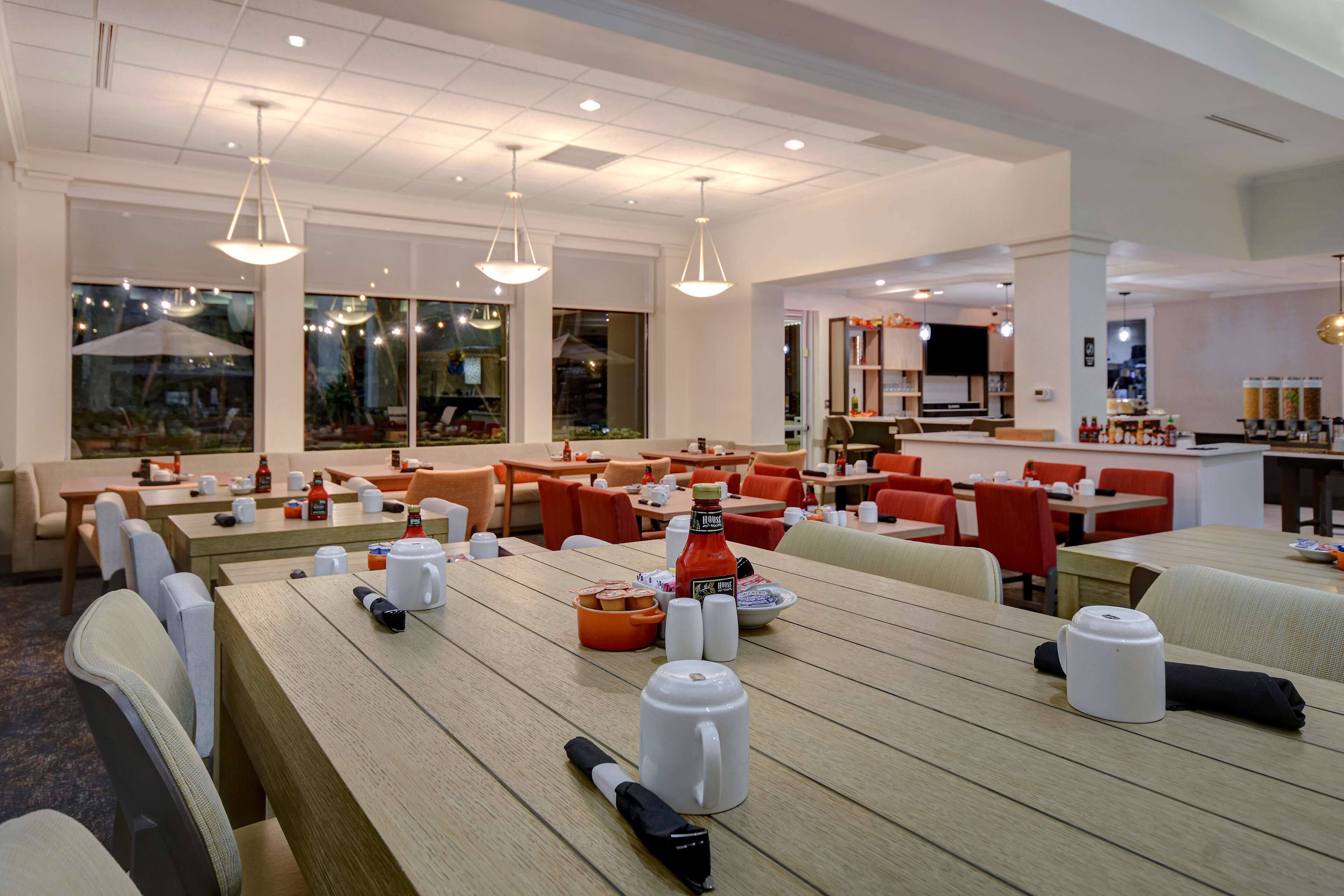 A modern dining area with wooden tables, chairs, and pendant lighting.
