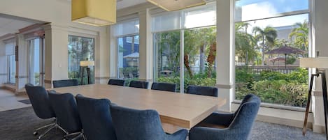 A conference room with a large table, six chairs, and large windows offering a view of palm trees and a building.