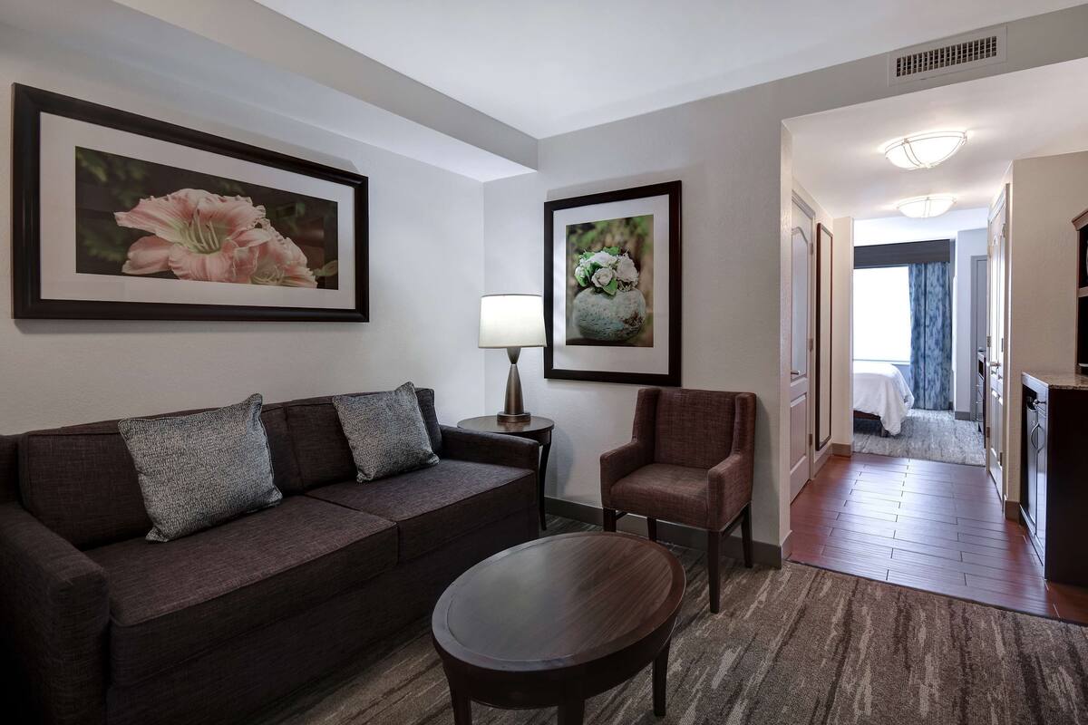 Ein Wohnzimmer mit einem dunkelbraunen Sofa, einem runden Couchtisch und zwei gerahmten Blumenbildern an der Wand.
