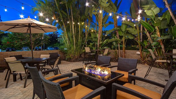 An outdoor patio with wicker furniture, a fire feature, and string lights. - Hilton Garden Inn Ft Myers (Fort Myers)