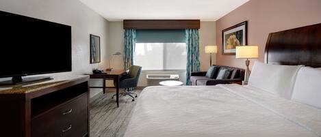 A hotel room with a large bed, a desk with a chair, a television, and two lamps.