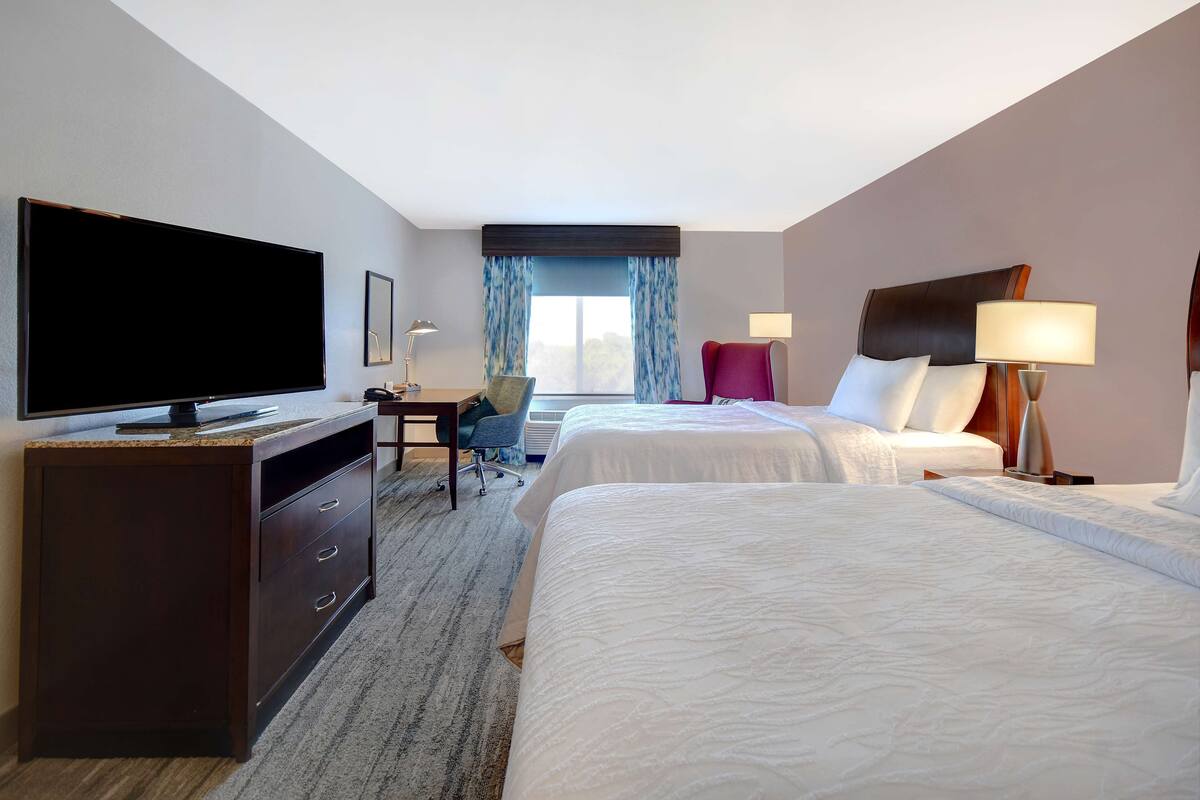 Ein Hotelzimmer mit zwei Betten, einem Fernseher, einem Schreibtisch und einem Stuhl.
