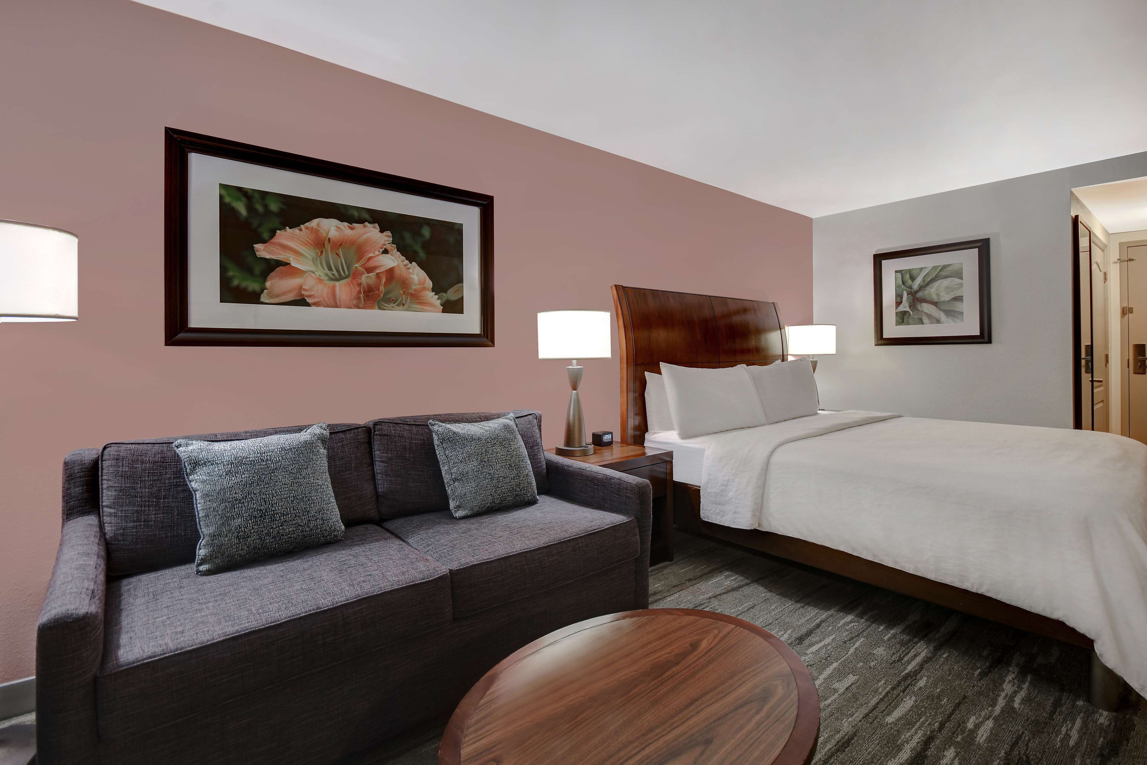 Quarto de hotel com cama, sofá, mesa redonda e duas luminárias fixadas na parede.
