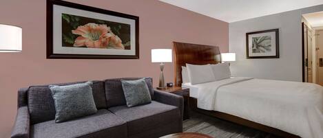 A hotel room with a bed, a sofa, a round table, and two wall-mounted lamps.