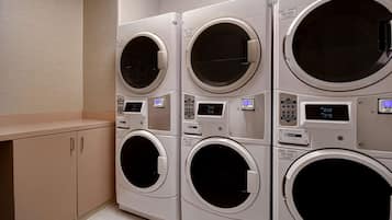 A row of four stacked front-loading washing machines in a laundry room.