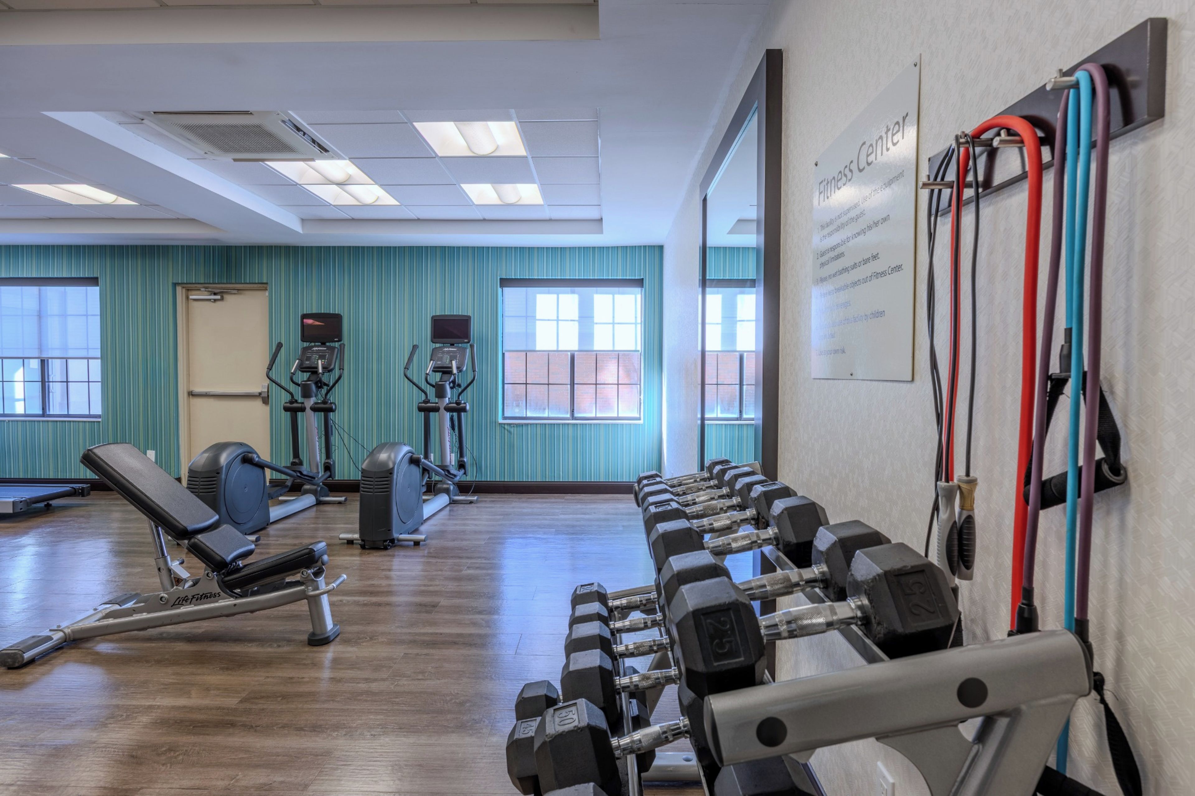 Un gimnasio con equipo de ejercicio, ventanas amplias y un letrero que indica que es un centro de acondicionamiento físico.