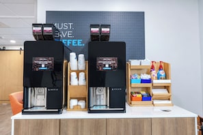 A coffee station with two espresso machines, a coffee cup display, and a shelf with coffee products. - Holiday Inn Express Hotel & Suites Columbus SW-Grove City by IHG (Grove City)