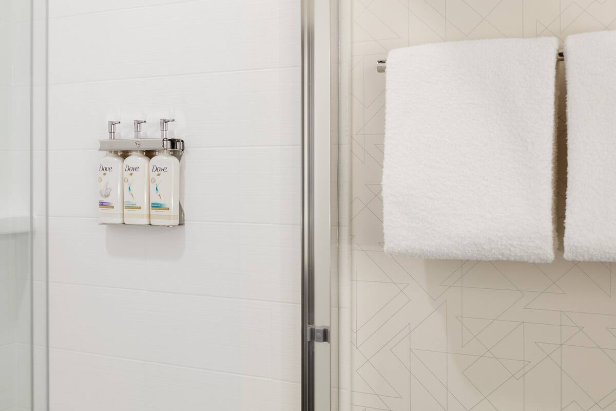 A bathroom with a shower, a towel rack with two towels, and three Dove body wash bottles on a wall.