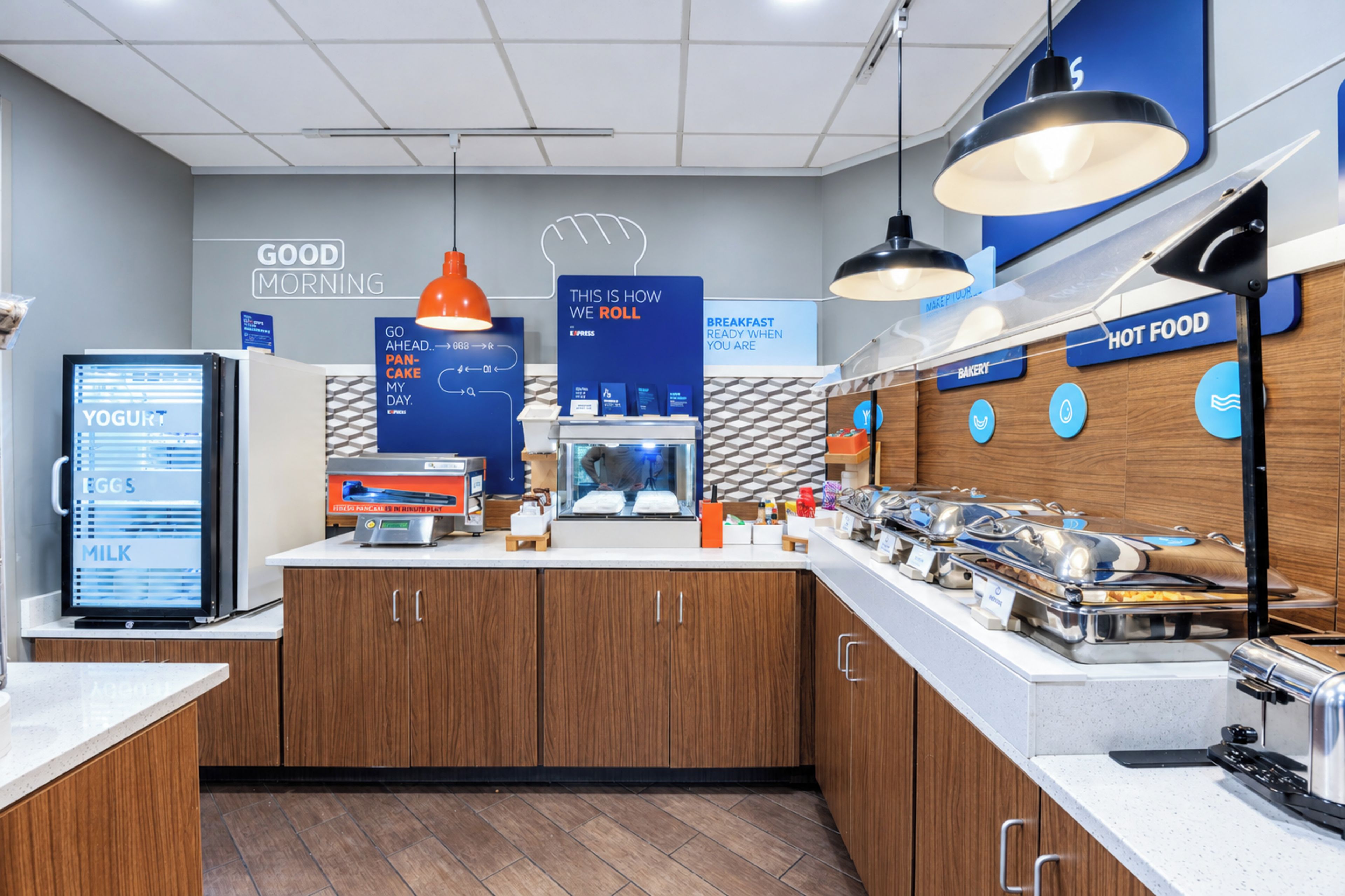 A breakfast area with a refrigerator, a coffee machine, and a buffet with various food options.