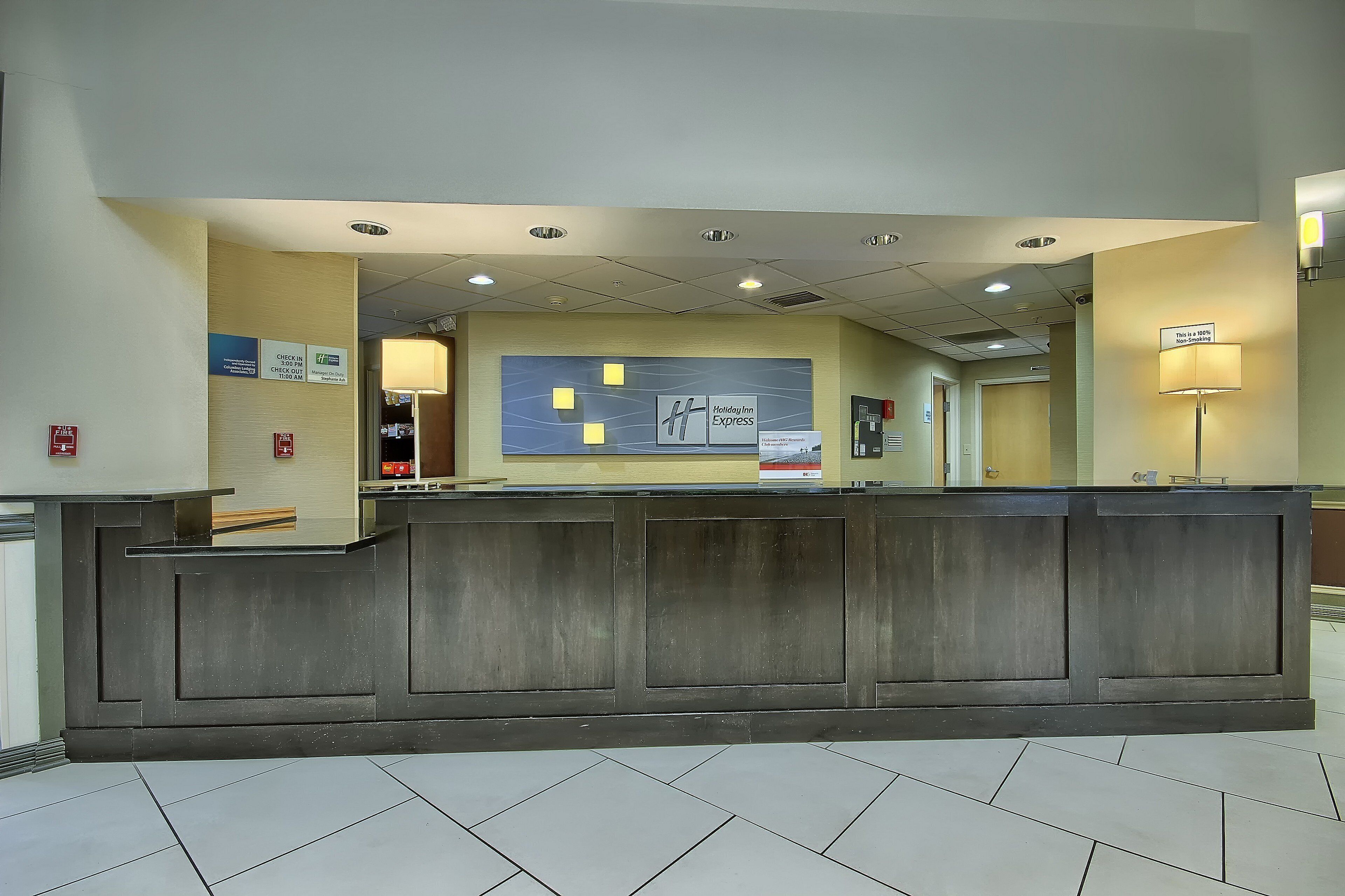 A hotel reception desk with a check-in/check-out counter, a fire alarm, and a non-smoking sign.