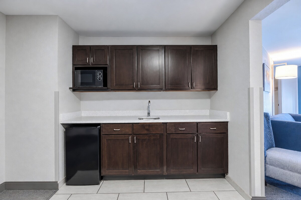 A compact kitchen with dark wooden cabinets, a built-in microwave, and a dishwasher.
