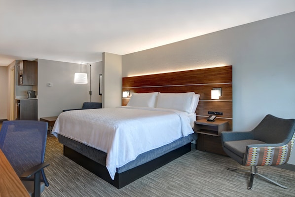 Une chambre d’hôtel moderne, dotée d’un grand lit, d’un bureau avec une chaise, d’une petite table et d’une table de chevet avec une lampe.