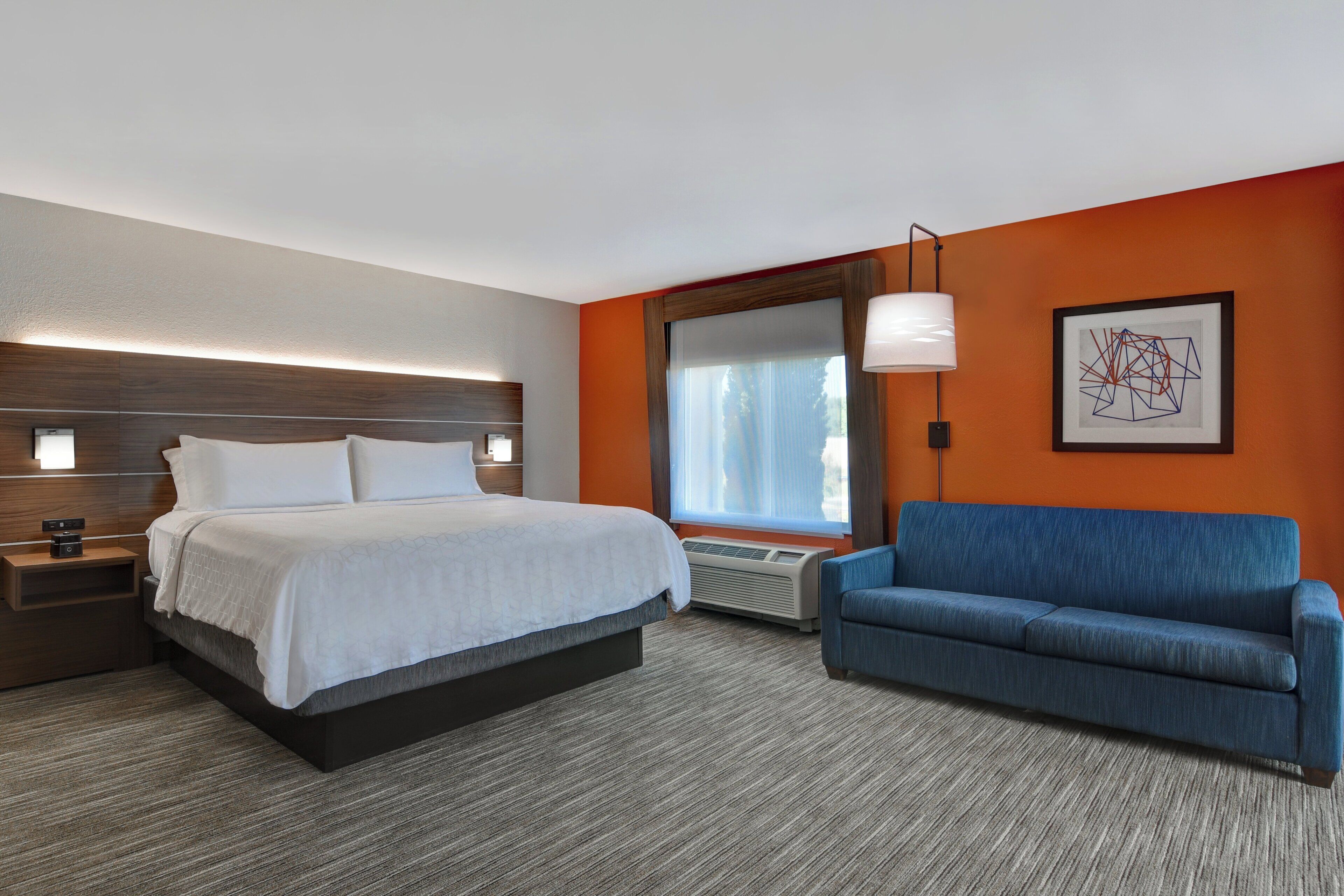 Ein Hotelzimmer mit einem Bett, einem blauen Sofa, einem großen Fenster und einem an der Wand hängenden Kunstwerk.