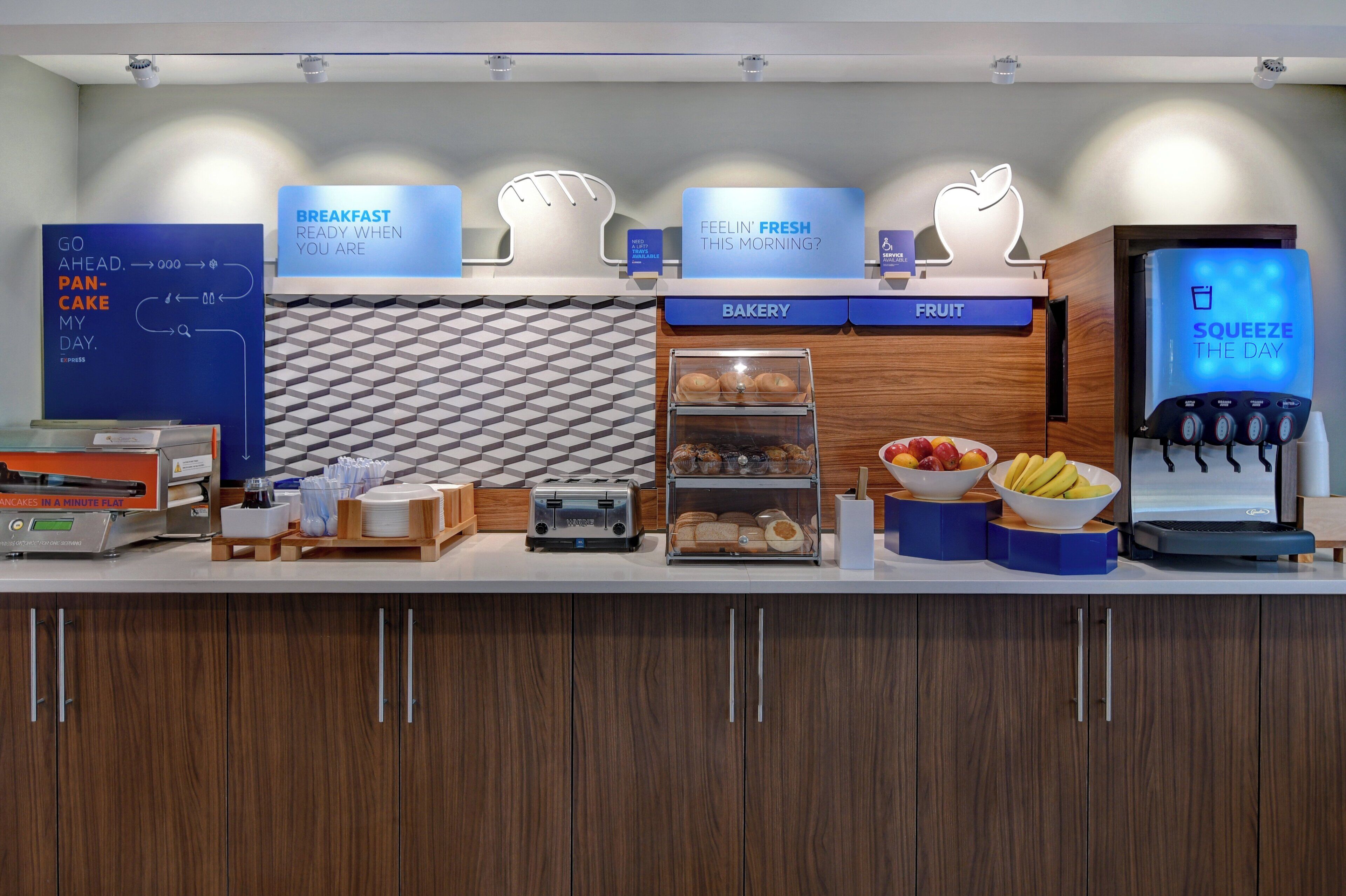 Un coin petit-déjeuner avec un grille-pain, un panier de fruits et une vitrine de pâtisseries.