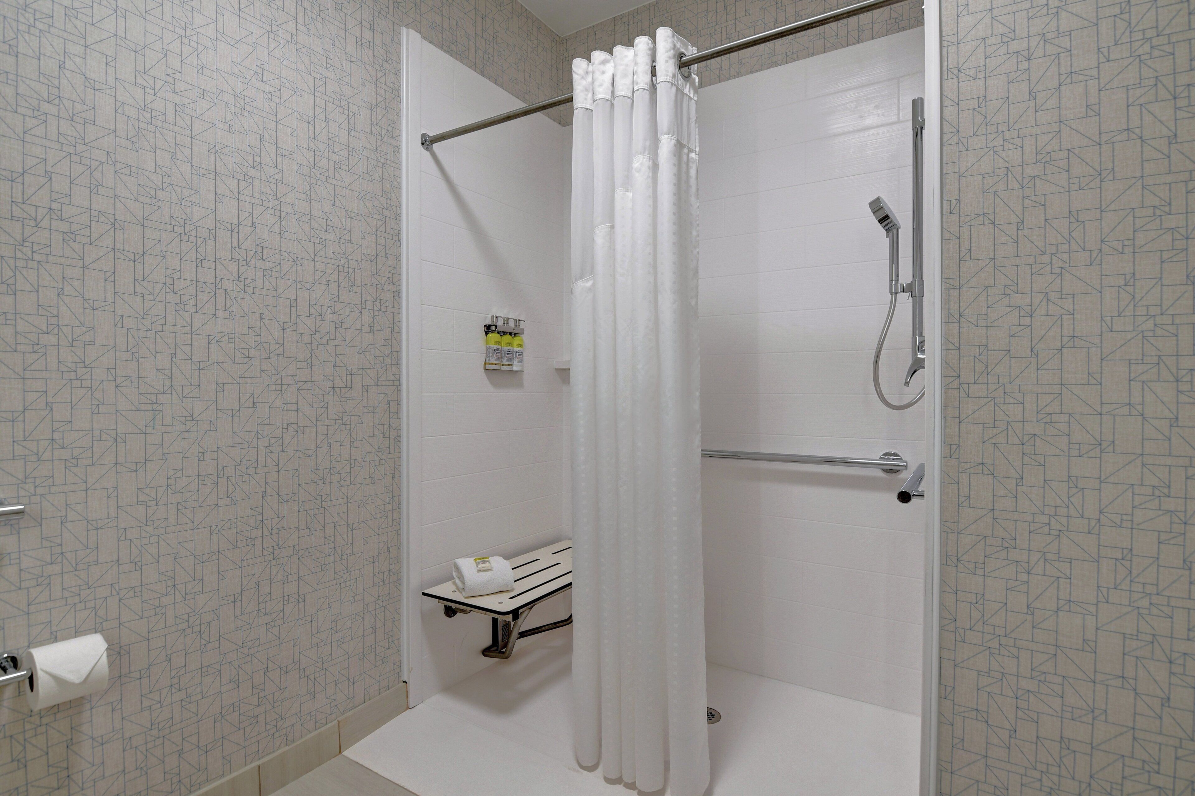 A shower with a white curtain, a handheld showerhead, and a towel rack with a towel.