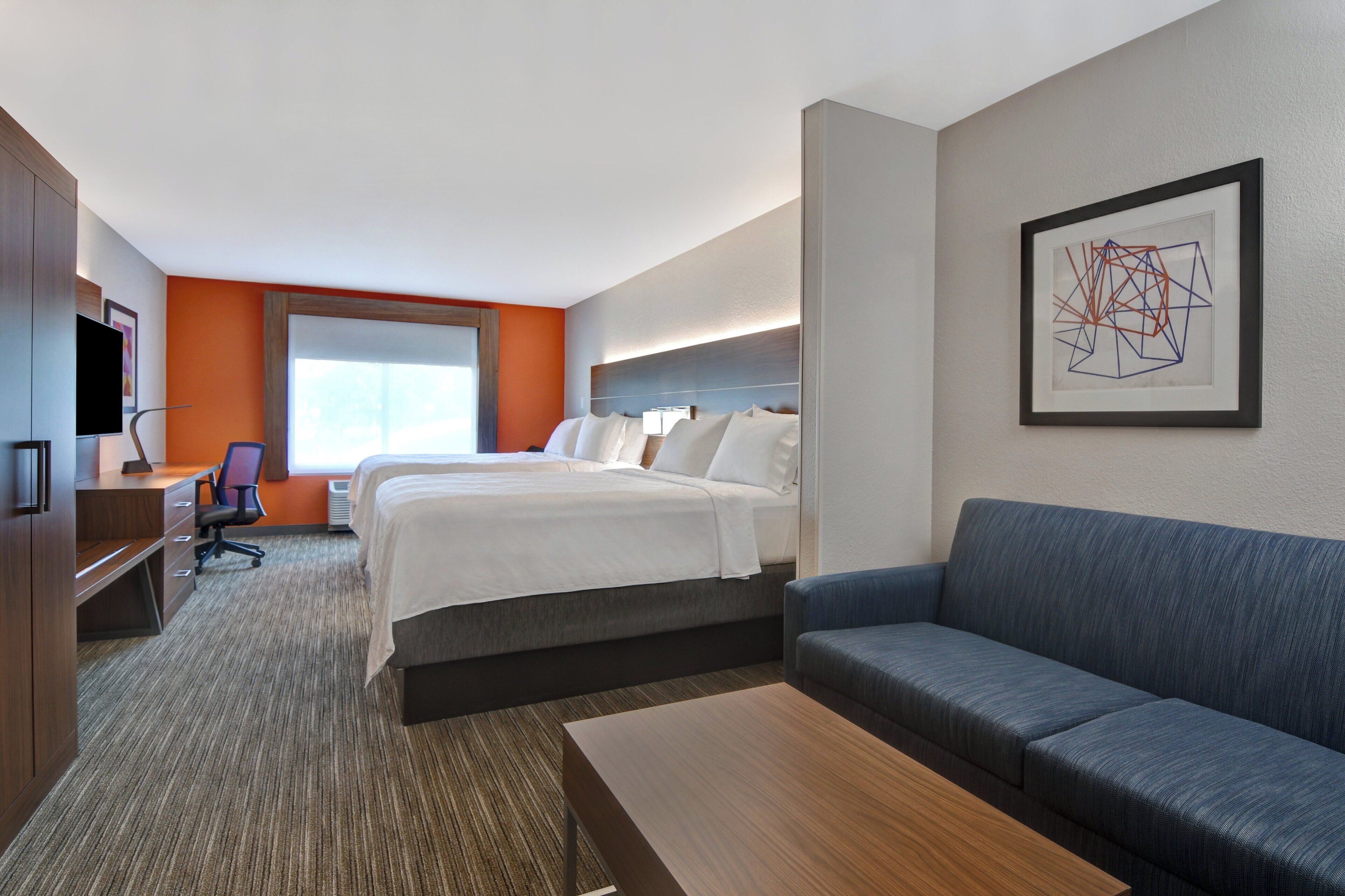 A hotel room with a bed, a desk, a chair, a sofa, and a painting on the wall.
