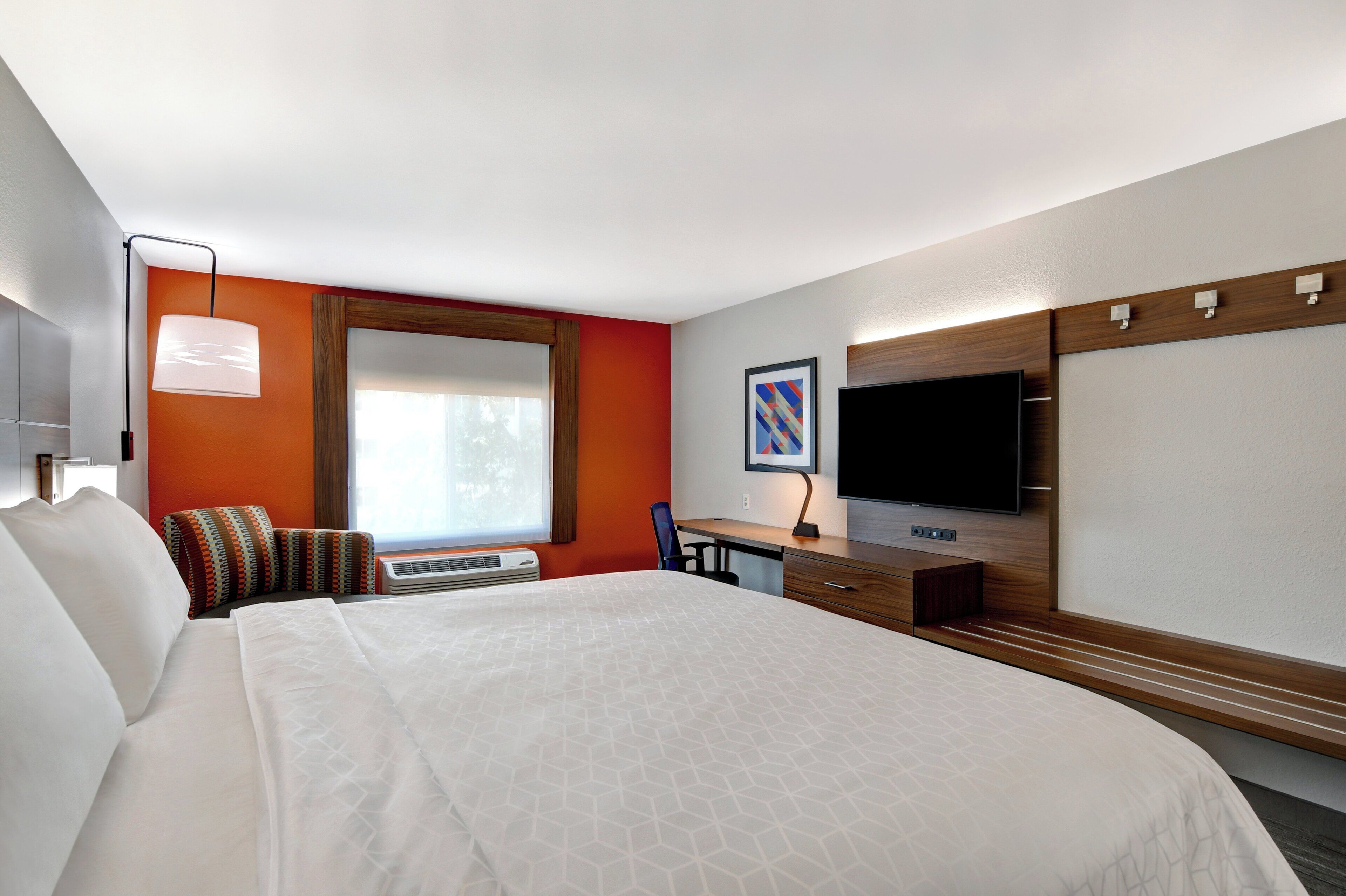 Habitación de hotel con una cama grande, escritorio, televisor de pantalla plana y ventana con cortinas.