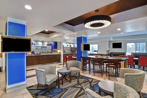 Un hall d’hôtel moderne doté d’un bar, de coins salon et d’un téléviseur.