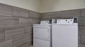 Un lavadero con dos lavadoras y secadoras apiladas, paredes de azulejos grises y piso de color claro.