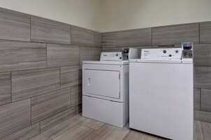 A laundry room with two stacked washers and dryers, grey tiled walls, and a light-colored floor.
