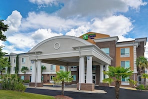 Un hôtel Holiday Inn Express & Suites doté d’une architecture moderne, avec une entrée imposante ornée de colonnes et un toit plat.