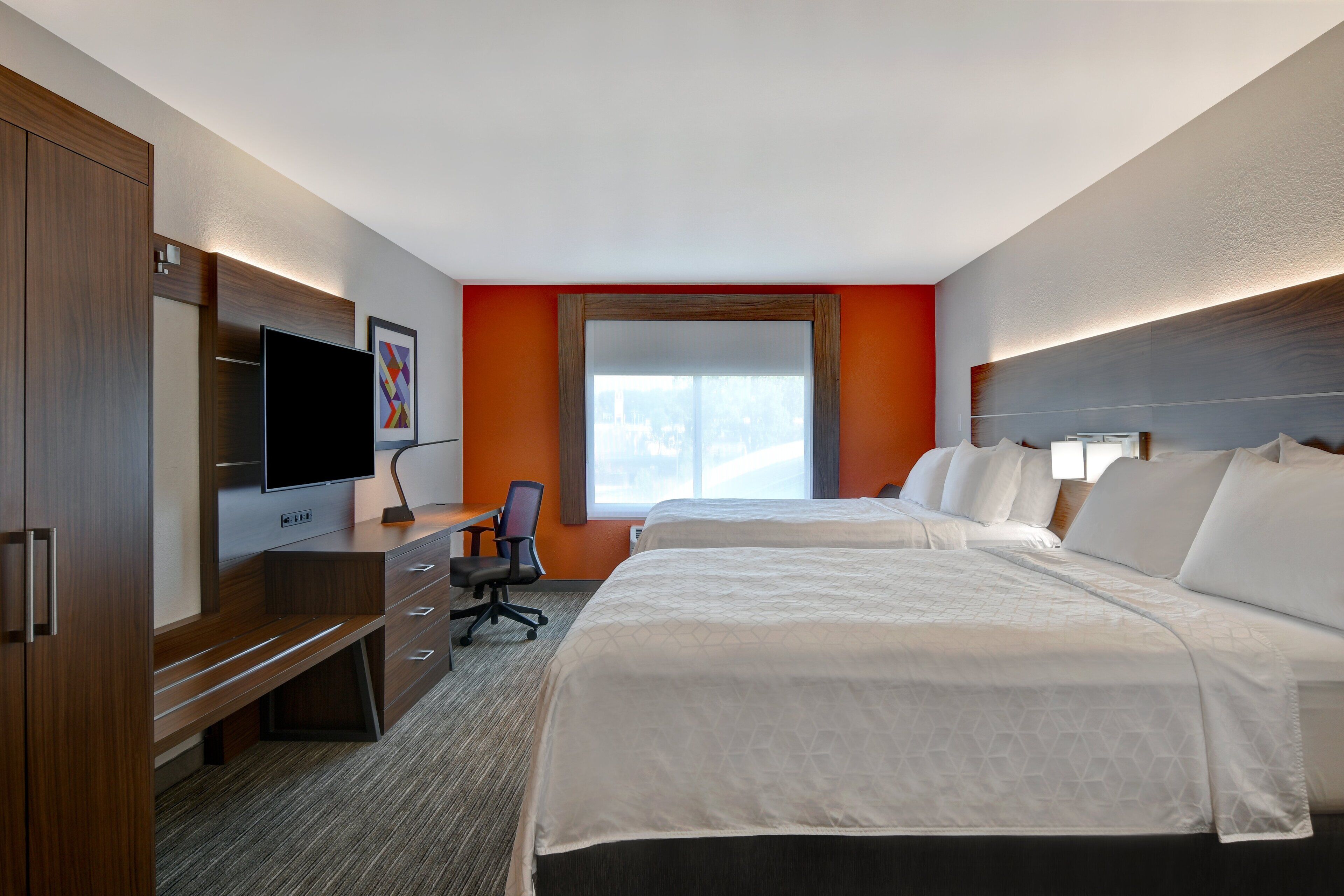 A hotel room with two beds, a desk with a chair, a TV, and a large window.