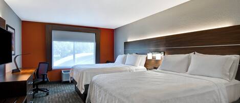 A hotel room with two beds, a desk, a chair, a television, and a window with a view of a road.