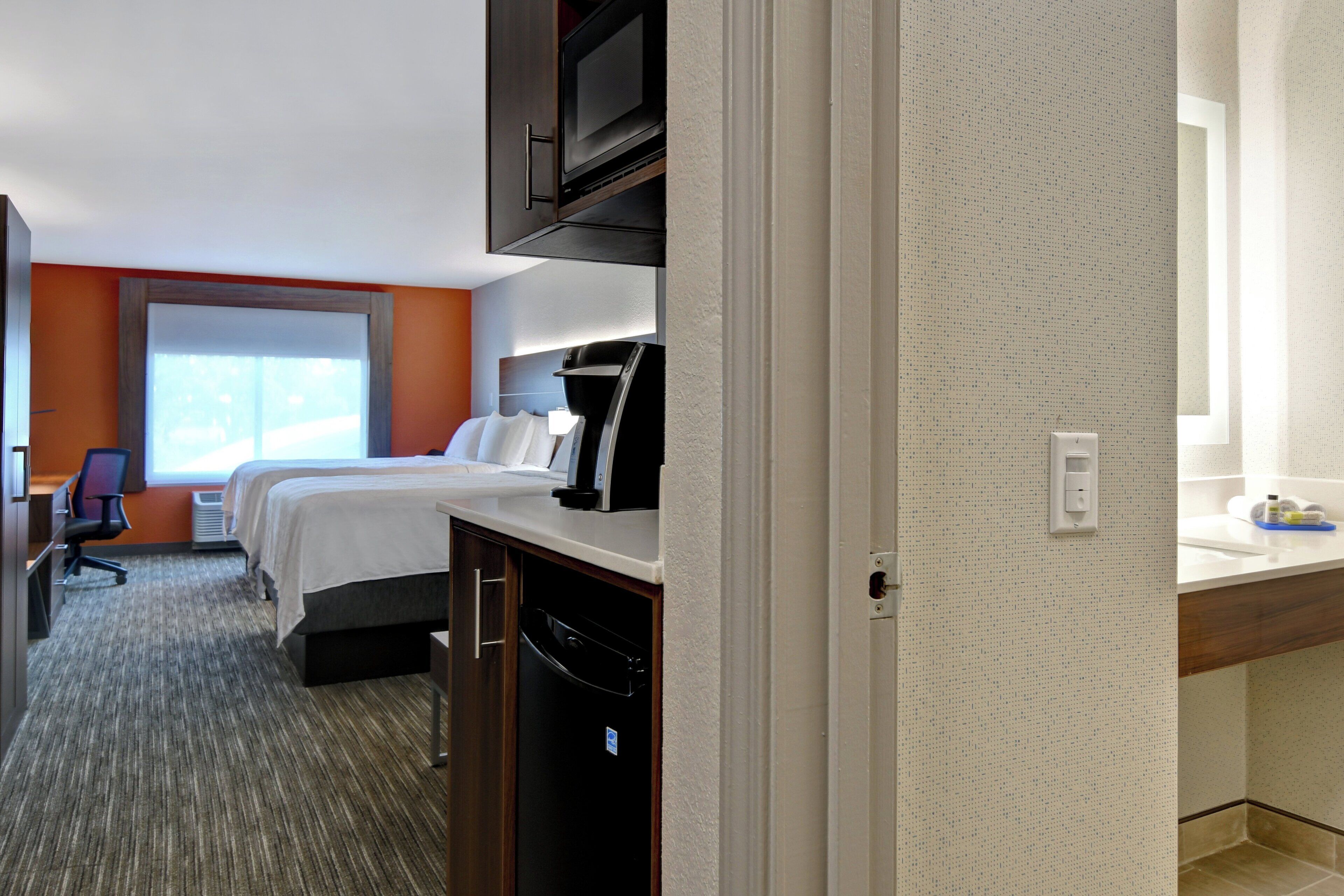 A hotel room with a bed, a desk, a chair, a TV, and a window.