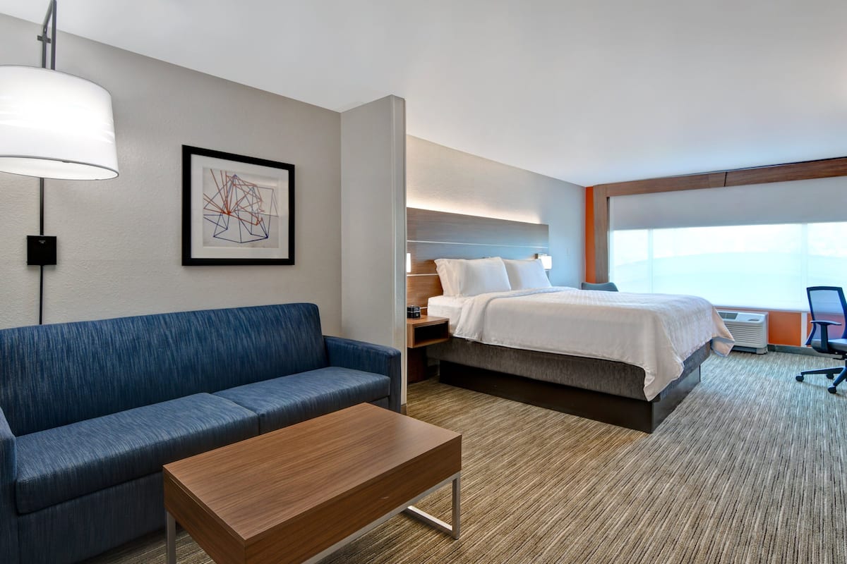 A hotel room with a bed, a blue sofa, a wooden table, and a framed abstract artwork on the wall.