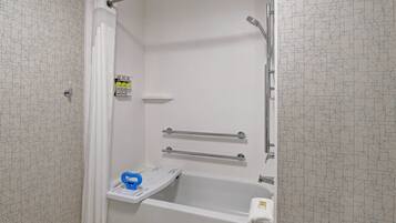 A bathroom with a shower, grab bars, a white bathtub, and a towel rack.