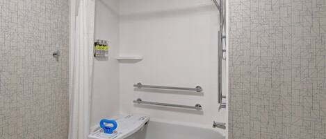 Een badkamer met een douche, grepen, een wit bad en een handdoekrek.