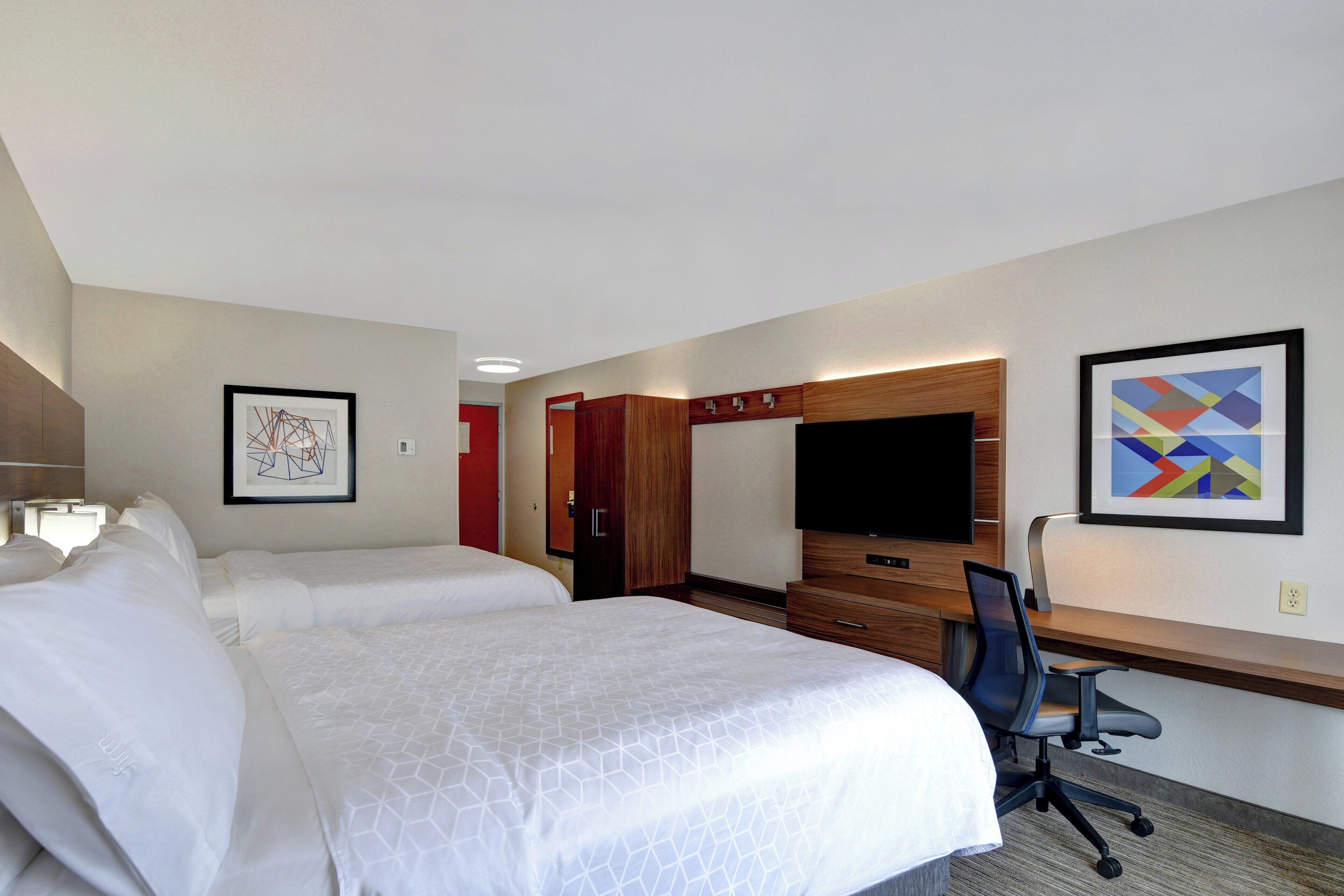 Een hotelkamer met twee bedden, een bureau, een stoel, een televisie en kunst aan de muren.