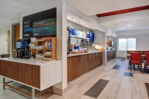 Interior moderno de una cafetería con una máquina de café, una barra con varios productos y una zona de estar con sillas rojas.