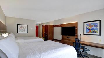 Ein Hotelzimmer mit zwei Betten, einem Schreibtisch, einem Stuhl, einem Fernseher und Bildern an der Wand.