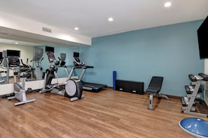 Une salle de sport équipée de matériel d’exercice, avec un miroir et un mur bleu.